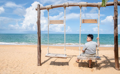 Rear view of woman sitting on chair at beach against sky