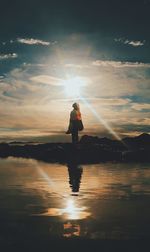 Silhouette young woman standing at beach against sky during sunset