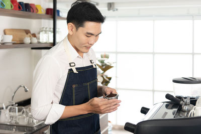 Asian barista man holding a coffee tamper in the coffee shop