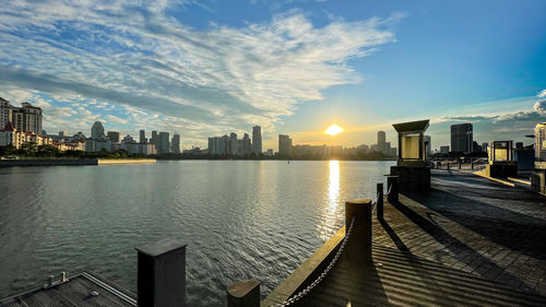 Scenic view of river by buildings against sky during sunset