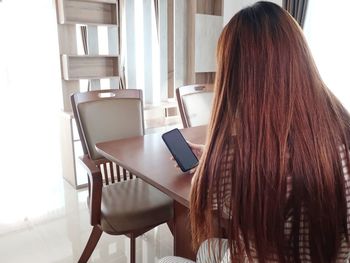 Rear view of woman using mobile phone at home