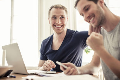 Happy loving homosexual couple with laptop siting at table in home