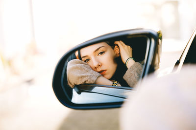 Portrait of young woman sitting on car window