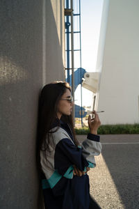 Young woman wearing sunglasses standing against wall