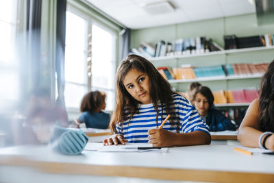 Portrait of girl with long hair giving educational exam while sitting in classroom at elementary school