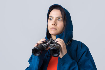 Portrait of young woman holding camera against white background