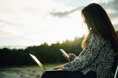 Side view of woman using mobile phone against sky