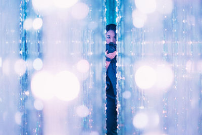 Portrait of woman photographing though digital camera seen through illuminated lighting decoration