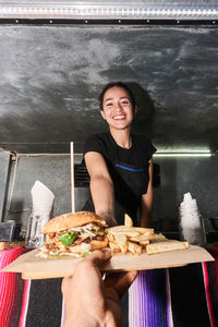 Hand of faceless unrecognizable buyer getting order with fast food from happy ethnic saleswoman at truck counter