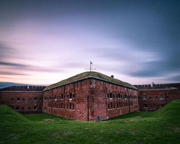 Building on field against sky at sunset