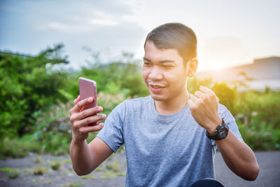 Man clenching fist while using mobile phone against sky