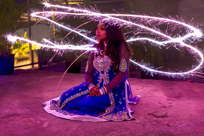 Young woman sitting amidst firework display at night