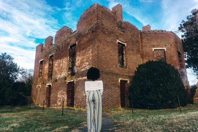 Rear view of man standing by old building against sky