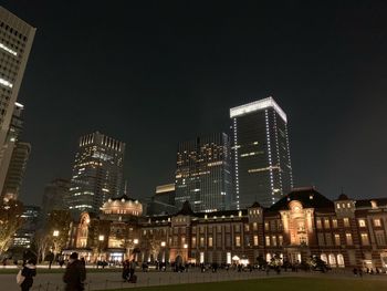 Illuminated modern buildings in city against sky at night