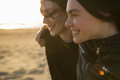 Happy female friends standing at beach during sunset