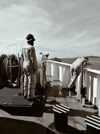 Workers working on boat in sea against cloudy sky