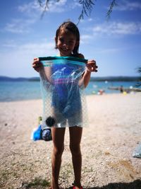 Full length of smiling girl carrying sea urchin in plastic bag at beach