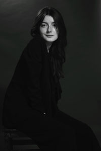 Portrait of young woman sitting against black background