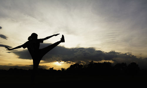 Silhouette woman standing on field against sky during sunset