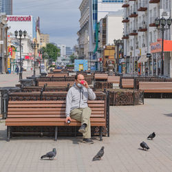 Man sitting on bench against buildings in city