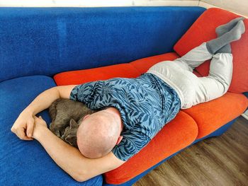 High angle view of man relaxing with cat on sofa at home