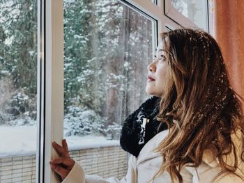 Side view of woman looking through window