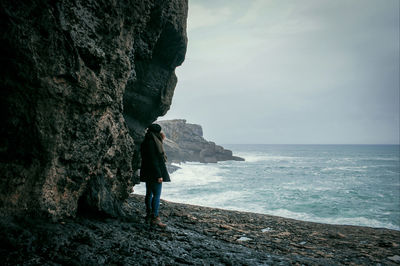 Woman standing on rock by sea against sky