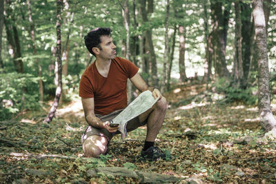 Man reading map while crouching in forest