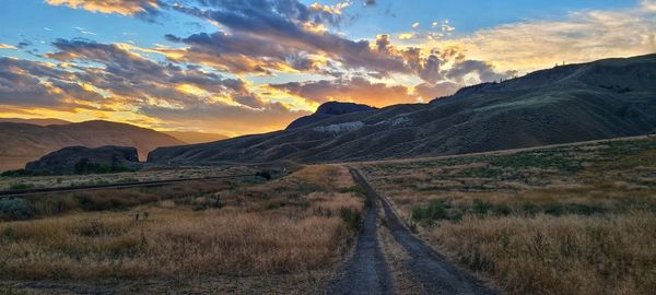 Road amidst field against sky during sunset