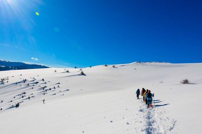 People hiking on snowy landscape against clear sky
