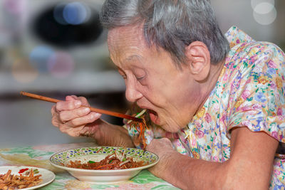 Close-up of senior woman eating food sitting at home