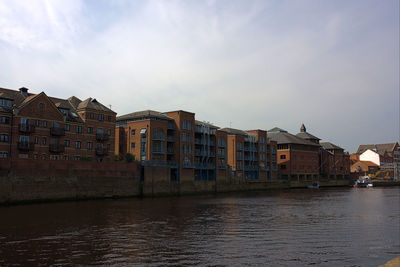 Buildings by river against sky in city