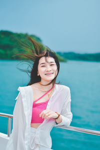 Portrait of young woman standing against lake