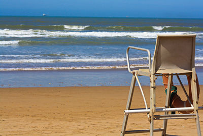 Chair on beach by sea against sky