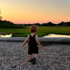 Full length of boy standing on beach against sky during sunset