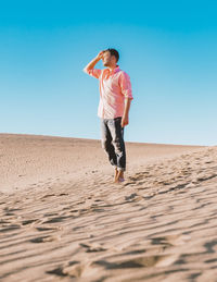 Full length of young woman standing at beach against clear blue sky