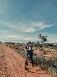 Full length of woman standing with bicycle on dirt road against sky