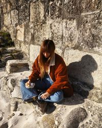 Full length of woman eating food while sitting on rock