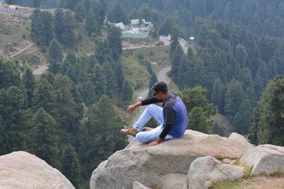 Side view of man sitting on cliff against trees