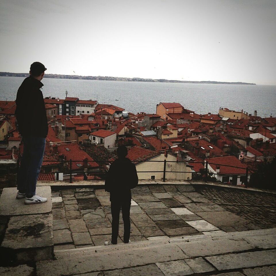 REAR VIEW OF MAN STANDING AGAINST BUILT STRUCTURES