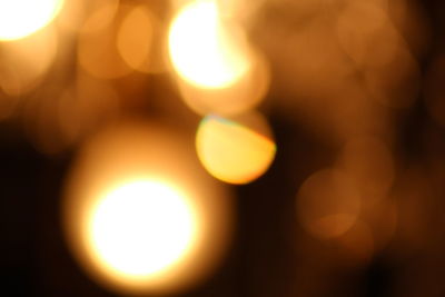 Defocused image of illuminated lights against sky during sunset