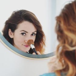 Close-up of young woman with make-up brush in front of mirror