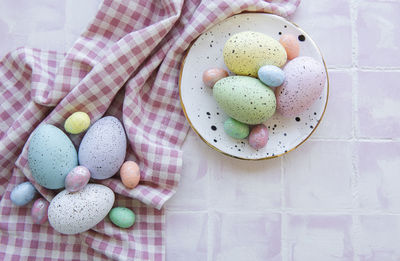 Colorful easter eggs on plate on pink tile background top view