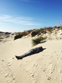 Full length of woman wearing warm clothing while lying on sand at beach against sky