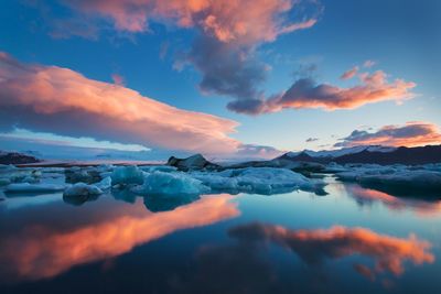 Scenic view of lake against dramatic sky during sunset