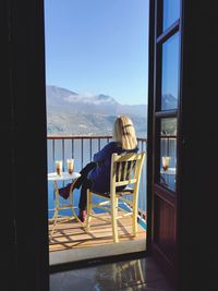 Man sitting on chair by window against sky