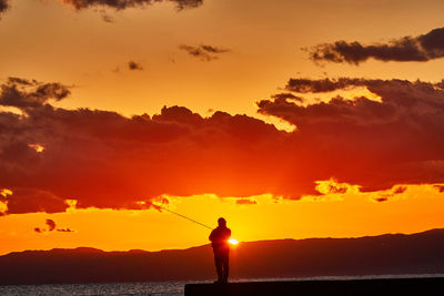 Silhouette man standing by sea against orange sky during sunset