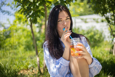 Portrait of young woman drinking water in park