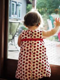 Rear view of girl standing by window at home