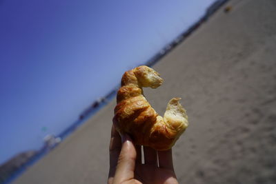 Close-up of hand holding ice cream cone at beach against sky